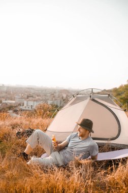 Genç bir adam çadırın yanında oturuyor ve internetten bir şeylere bakıyor.