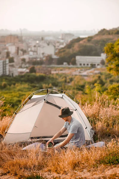 Egy férfi turista ül a sátor mellett és készíti az ételét. — Stock Fotó
