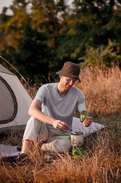 Мужчина-турист сидит возле палатки и готовит еду. — стоковое фото