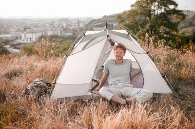 Kızıl bir adam çadırın yanında oturuyor ve uykulu ve rahat hissediyor.
