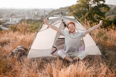 Kızıl bir adam çadırın yanında oturuyor ve uykulu ve rahat hissediyor.