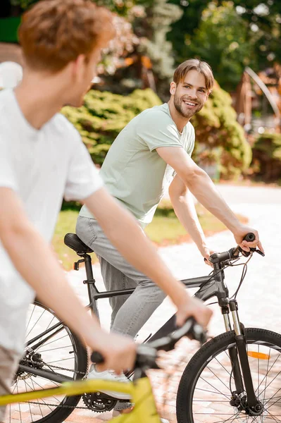 Deportista alegre y su amigo montando bicicletas en un parque — Foto de Stock