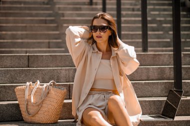 Güneş gözlüklü genç bir kadın merdivenlerde oturuyor.