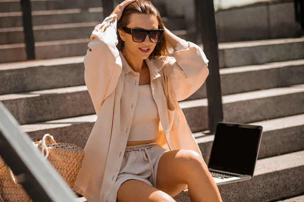 A young stylish woman in sunglasses sitting on the steps — Stock Photo, Image