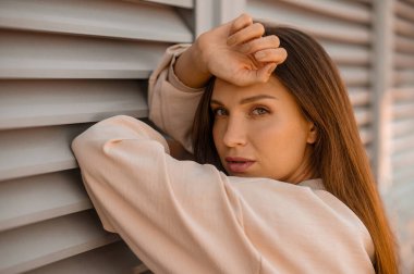 Duvarın yanında bej renkli güzel bir kadın resmi.