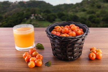 Acerola suyu ve doğadaki ahşap masada çiğ aserolas.