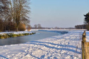 Hollanda 'da donmuş bir kanal manzarası. Mavi bir kış gökyüzünün altında.