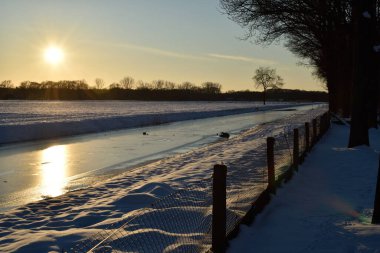 Donmuş bir Hollanda kanalı ve yol silueti Kış günbatımında