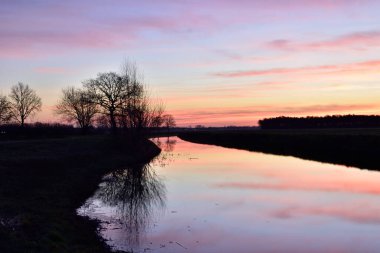 Hollanda 'da Vinkel' e yakın bir kanalda şafak vakti gökyüzü yansıyor.