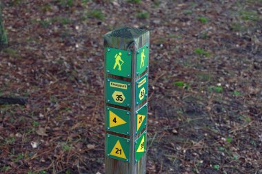 Yeşil zemin üzerinde sarı semboller ve oklar olan tahta yürüyüş işareti direği.