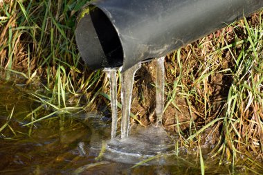 Aşağıdaki donmuş bir akıntıya düşerken buz saçaklarına dönüşen borudan akan su.
