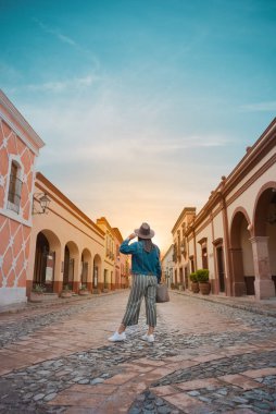 Tourist woman standing in the middle of the street of a magical town, town of La Pena del Bernal in Queretaro, Mexico, with sunset in front, summer day clipart