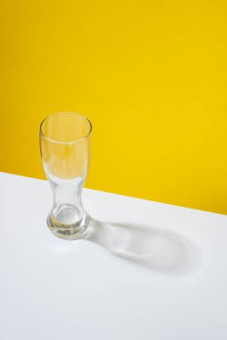 Sarı arka planda beyaz bir masaya yerleştirilmiş boş bir bira bardağı.