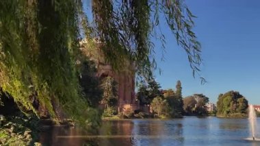San Francisco 'daki Güzel Sanatlar Sarayı' nın panoramik 4K el kamerası görüntüsü. Gün boyunca açık mavi gökyüzü altında neoklasik mimarinin arka planında güneşli su lagünü geçiyor.