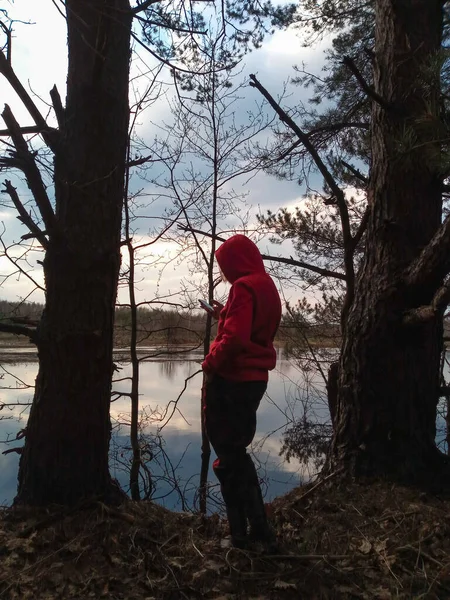 絵のように美しい川の岸に赤いジャケットの少女は 呼び出しを待っている携帯電話を保持しています — ストック写真