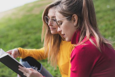 İki kadın açık hava parkında ilginç bir kitap okumaktan zevk alıyor.