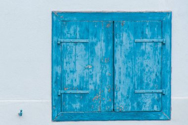 Kırsal mavi ahşap pencere panjurları, desenli beyaz bir binanın penceresini kapatıyor.