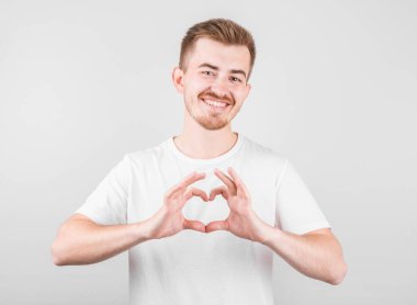 Gülümseyen genç adamın portresi ellerini göğsüne koyuyor. Kalp şeklinde bir işaret. Sempati gösteriyor.