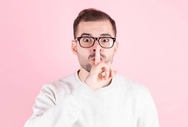 Pembe arka planda genç yakışıklı bir adam parmakları dudaklarında sessiz olmak istiyor. Sessizlik ve gizli konsept.