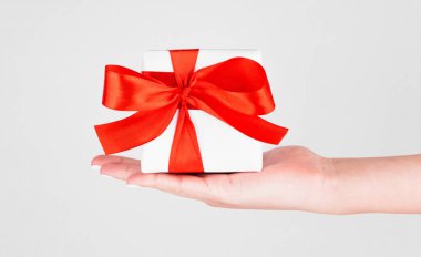 Sevgililer Günü için beyaz masada elinde kırmızı kurdele olan hediye kutusu.