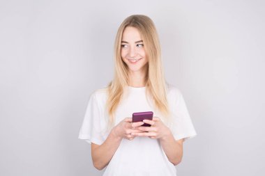 Beyaz duvarda izole bir şekilde cep telefonuyla sohbet eden neşeli ve güzel bir genç kadının fotoğrafı. Takma uzaya bakıyorum..