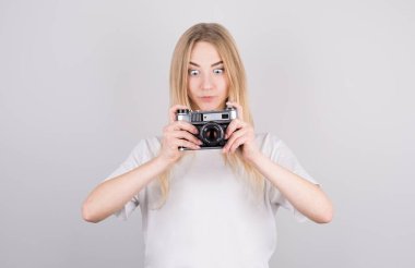 Stüdyoda gri bir arka planda beyaz tişörtlü güzel, genç, şaşkın, sarışın bir kadının etkileyici portresi..