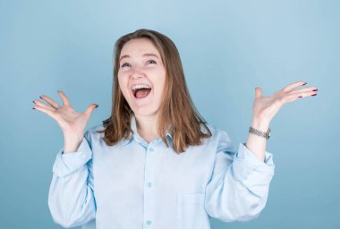 İzole edilmiş açık mavi arka planda duran şaşırmış genç kadın görüntüsü.