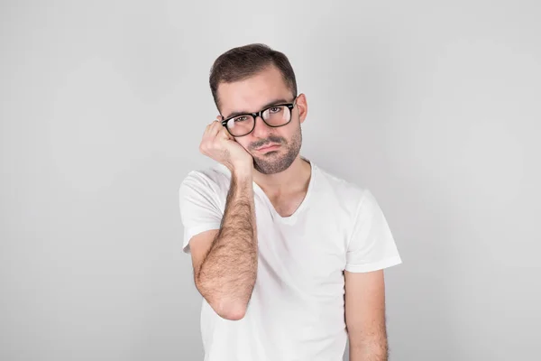 stock image Studio shot of an annoyed annoyed handsome guy in black glasses who touches his face and bends over, looks out from under his eyes, hates talking to a boring person, stands against a gray background