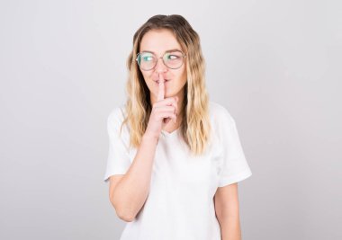 Genç bir dişi, sessiz olmak istiyor. Parmağı dudaklarında, bir de yana bakıyor. Pembe arka planda sessizlik ve gizli konsept