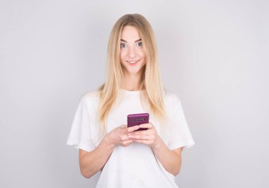 Elinde cep telefonu olan ve beyaz arka planda izole edilmiş kameraya bakan şaşırmış çekici bir kızın portresi.