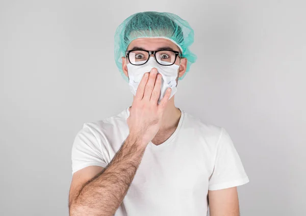 白い医療用マスクと医療用キャップの医師外科医は 手で手を閉じて 驚きと白い背景の上に立っています 19歳の時インフルエンザと季節の寒さが — ストック写真