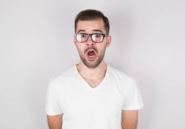 Gri arka planda beyaz fanila giyen gözlüklü adam şaşırdı.