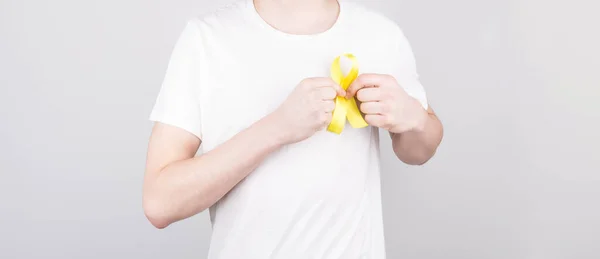 Young man in white t-shirt holding yellow ribbon awareness symbol for suicide, sarcoma bone cancer, bladder cancer, liver cancer and childhood cancer concept. Health care.