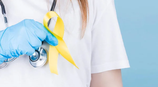 Young female in white t-shirt holding yellow ribbon awareness symbol for suicide, sarcoma bone cancer, bladder cancer, liver cancer and childhood cancer concept. Health care.