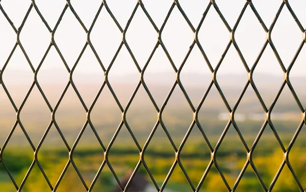 El fondo es bokeh paisaje detrás de la malla de alambre . — Foto de Stock