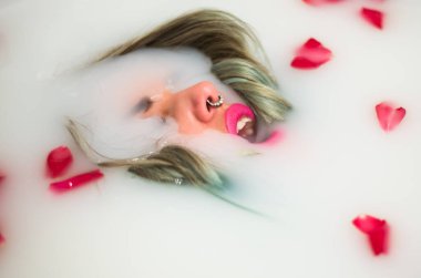 Piercingli güzel bir kadın rahatlatıcı bir süt ve gül banyosu yapıyor.