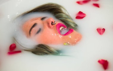 Piercingli güzel bir kadın rahatlatıcı bir süt ve gül banyosu yapıyor.