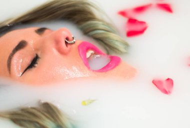 Piercingli güzel bir kadın rahatlatıcı bir süt ve gül banyosu yapıyor.