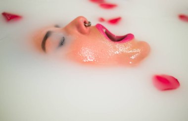 Piercingli güzel bir kadın rahatlatıcı bir süt ve gül banyosu yapıyor.