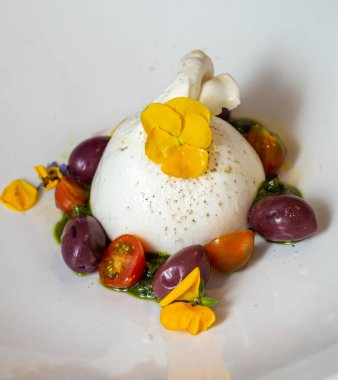 Peynirli mozarella salatası. Eşek sütü, kiraz rengi domates ve fesleğen. Hepsi bir gurme restoranından alınmış beyaz bir tabakta.