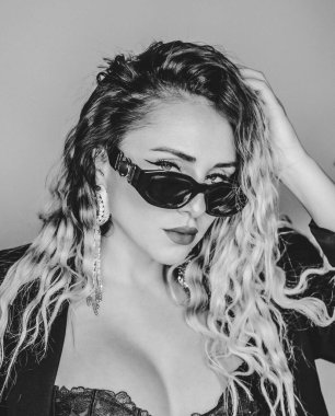 Alternatif bir modelin siyah beyaz portresi. Sarı kıvırcık saçlı, güneş gözlüğü takan.