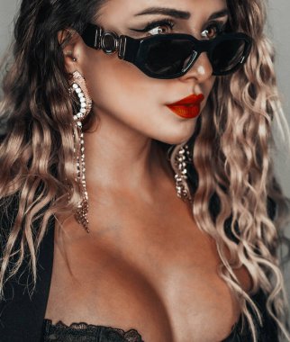 Güzel kıvırcık saçlı, güneş gözlüklü, tahrik edici pozlarda sarışın bir kadın.