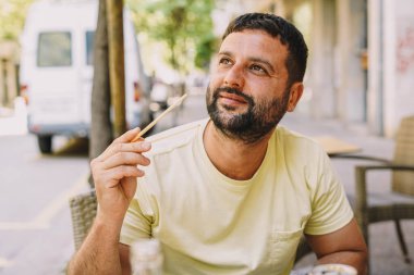 Latin adam terasta oturmuş suşi ve Japon eriştesi yiyor.
