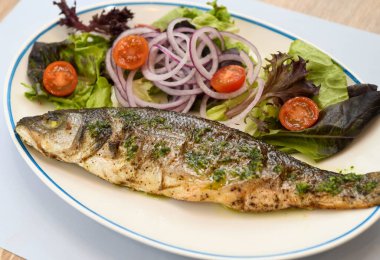 Beyaz tabakta salata ve soğanlı ızgara deniz kabuğu.