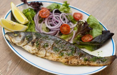 Beyaz tabakta salata ve soğanlı ızgara deniz kabuğu.