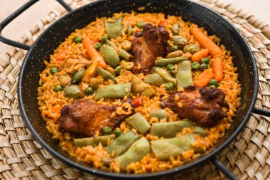 Hasır bir tabakta etli, pirinçli ve sebzeli paella.