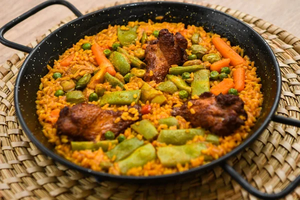 Hasır bir tabakta etli, pirinçli ve sebzeli paella.