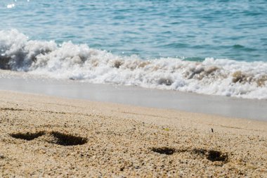 Kumsaldaki ayak izleri, arka planda deniz, sahil