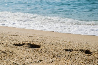 Kumsaldaki ayak izleri, arka planda deniz, sahil