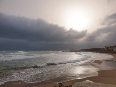 Sitges 'de kumsalda rüzgarlı bir gün, dalgalı denizli dramatik bir gökyüzü.